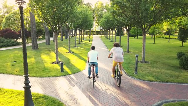 Two male friends riding bicycles in park. Young man cycling in summer park, drone view. Happy weekend with bikes.