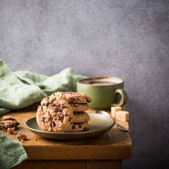 Stack of chocolate chip cookies on green plate with cup of coffee on old wooden table. Selective focus. Copy space.