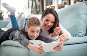 Mom and son using tablet together on sofa at home