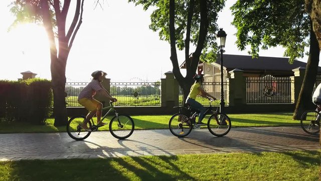 Four young persons cycling in public park. Group of young people riding bicycles along a road and looking happy. Enjoying summer day together.