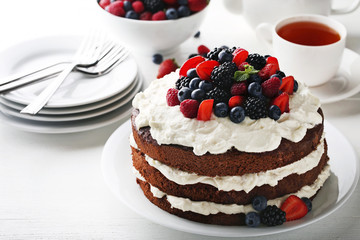 Delicious chocolate biscuit cake with cup of tea and plates on white wooden table