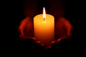 Female hands holding burning candle on black background