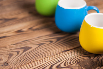 Row of colored empty ceramic clean mugs on old worn brown wooden table with copy space