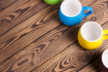 Row of colored empty ceramic clean mugs on old worn brown wooden table with copy space