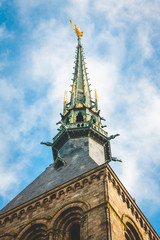 Low view close up of spire with statue of Archangel Michael against blue sky of abbey on Le Mont...