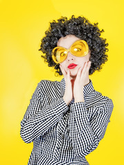 Surprised girl clown with afro wig, isolated on yellow background