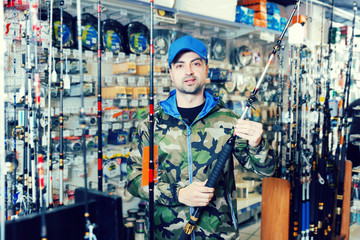 Obraz na płótnie Canvas Male customer in fishing clothing choosing fishing rod