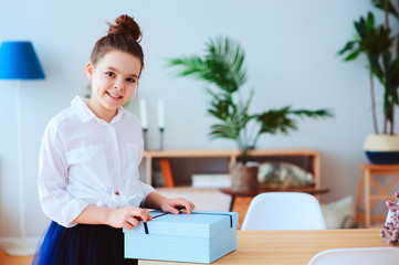 happy kid girl with gift for birthday or womans day posing at home in modern scandinavian interior, preparing or unwraping gift.