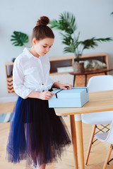 happy kid girl with gift for birthday or womans day posing at home in modern scandinavian interior, preparing or unwraping gift.