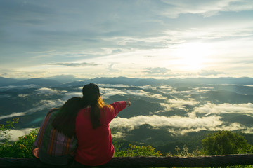 Fototapeta na wymiar Women sit on the wood branch and viewing scenery sunrise in the morning with green mountain and fog.