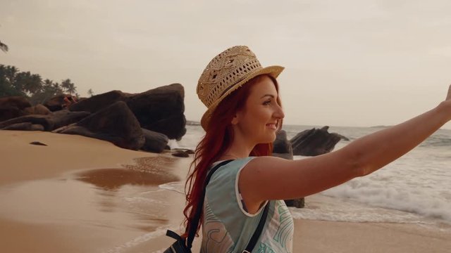 young red-haired woman tourist taking pictures using a smartphone sunset on the ocean beach, slow motion