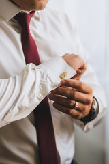 A man or businessman in a red tie zips his hands with a gold cufflink on a white shirt