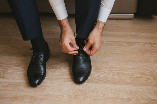 A Man Or Businessman In A Suit Ties Up Shoelaces On Black Leather Shoes On A Parquet Background