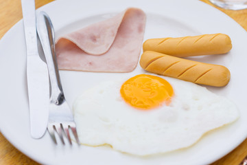 Close up breakfast with egg,ham and sausage in the white plate on the wooden table.