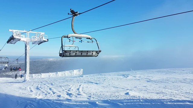 An ski lift going up a frozen and snowy mountain with blue sky above