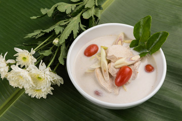 Thai coconut chicken soup (Tom Kha Kai) in bowl with herb on banana leaf
