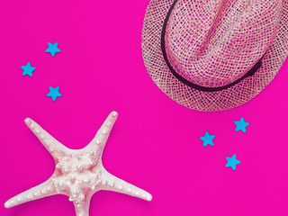 A hat knitted from straw and a large starfish are on a clean purple background. A few blue stars are scattered around. Image for advertisement of travel agency, party banner, rest and holiday