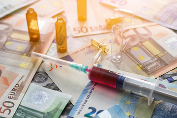Open vials of medication and a syringe on a background of money