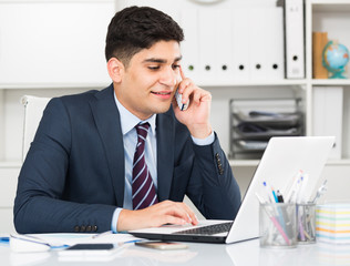 Young male is working at a computer and talking phone