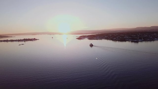 Aerial shot of a ferry boat in Oslo fjord, Norway, moving away from camera towards the sunset