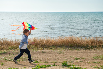 active happy kid running with colourful kite in his hands along sea shore in spring