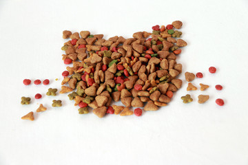 Heap of cat food set to cat face shape on the white floor. Cat food is food for consumption by cats. Cats have specific requirements for their dietary nutrients.