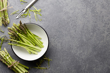 Peeling and cooking fresh raw asparagus on stone kitchen countertop, top view