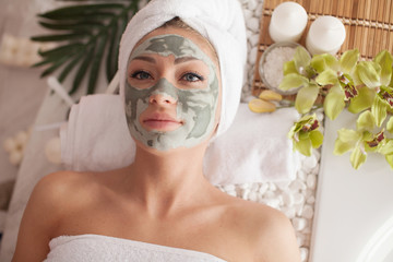 Young healthy woman in spa making treatments and face clay mask.
