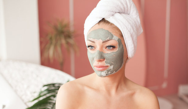 Young healthy woman in spa making treatments and face clay mask.