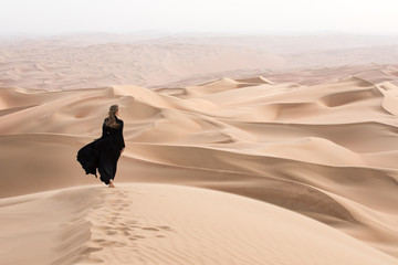Young beautiful Caucasian woman posing in a traditional Emirati dress - abaya in Empty Quarter desert landscape. Abu Dhabi, UAE. - obrazy, fototapety, plakaty