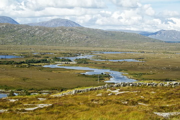 A landscape with mountains, meandering water and a stone wall.