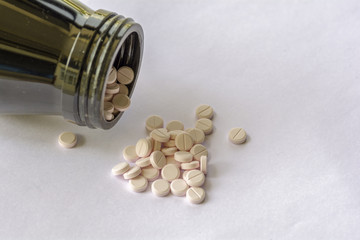 White pills from brown bottle on white background.