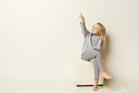 Happy little girl pointing aside at white studio background