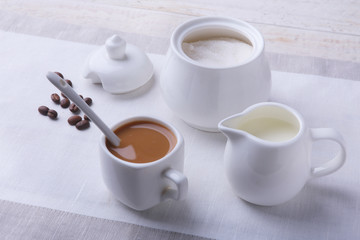 Cup of hot coffee espresso, coffee beans, jug of milk, and bowl with sugar on white background for copy space. Coffee concept.
