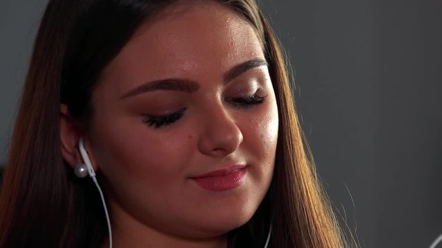 A young beautiful woman listens to music with a smile and earpieces in her ears, then takes them off - face closeup
