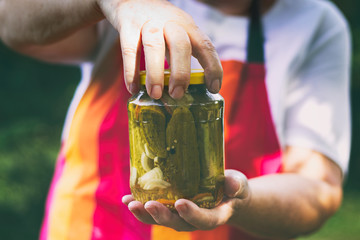 Senior woman holding a jar of pickles in the garden. Homemade pickled cucumbers in a glass jar....