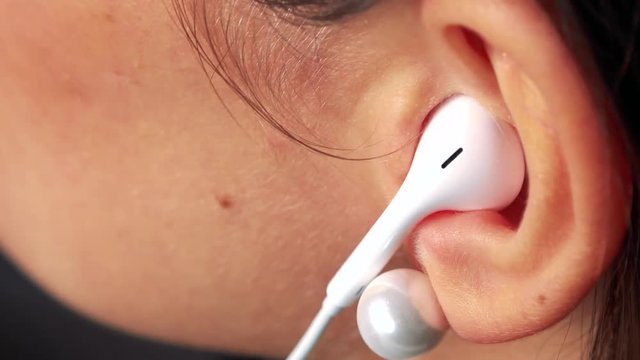 A woman puts earpieces in her ears and listens to music - ear closeup