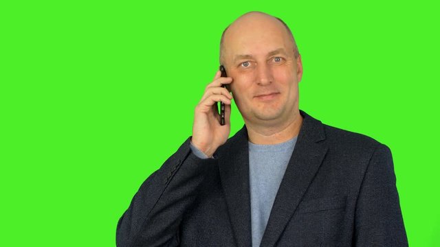 Bald caucasian man look to camera and hold smart phone at ear. Caucasian man talks by phone. Man speaking pn phone. Alpha channel, keyed green screen.