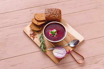 bowl of borscht with pieces of bread and onions on a wooden table