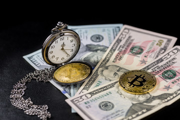Golden bitcoin lying on us dollars with pocket watch on black background