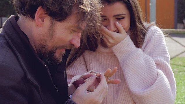 Handsome man putting engagement ring on finger of girlfriend happy slow motion closeup