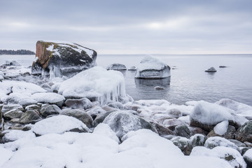 Rocky beach on wintertime. Evening light and icy weather on shore like fairy tale country. Winter on coast. Blue sky, white snow, ice covers the land on seaside. Waterside on Juminda, Estonia, Europe