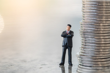 Money and Business Concept. Businessman miniature figure standing on ground with stack of silver coins.