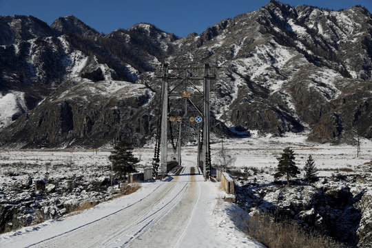 Fototapeta Metal bridge over river in front of snow mountain and blue sky
