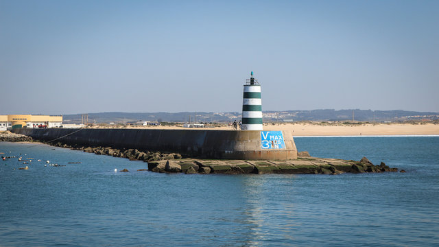 Jetty with a lighthouse in the entrance of a port with the beach in background. Peniche in Portugal