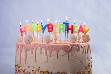 pink white cake with coconut balls and happy birthday candles 