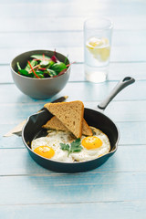 Breakfast table. Fried egg in frying pan on blue wooden table with salad and lemon water