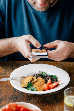 Man takes pictures of vegetarian food that he eats (black quinoa and cutlets from oatmeal and prunes). Healthy vegetarian food concept