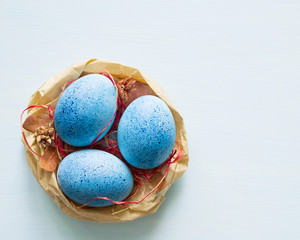 Blue Easter eggs in a decorative paper nest on light blue background, top view, copy space