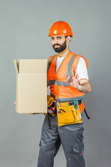 A man-builder in an orange helmet with a cardboard box in his hands. On a gray background